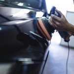 Hands with orbital polisher in auto repair shop. Selective focus.