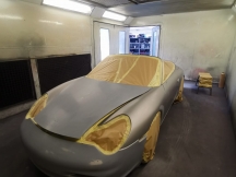 Car in spray booth prepared to be resprayed, taped with paper to protect windows, wheels and lights