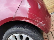 Red car with scratches on rear wheel arch and bumper