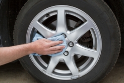 Man's hand with rag cleaning a dusty car wheel disk in the garage. Early spring washing or regular wash up. Professional car wash by hands.