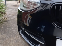 Black car front bumper and headlight on customer driveway