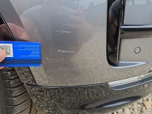 Grey car with scratch on front bumper with card to show size