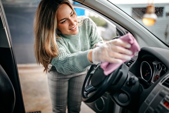 woman cleaning the interior of a car with a pink cloth and gloves