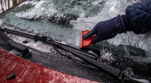 Hand Close Up cleaning the ice down the windscreen from the snowy car